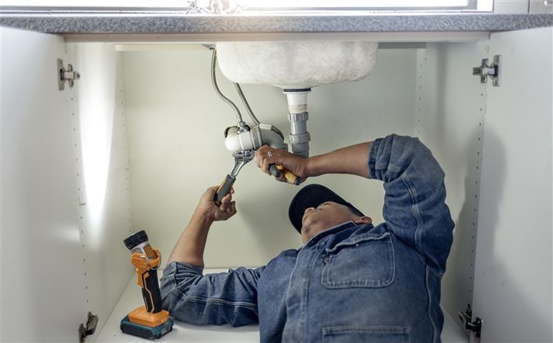 Plumber repairing pipes beneath a bathroom sink in Menlo Park